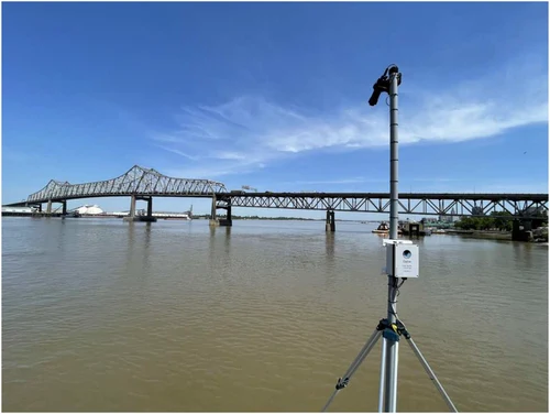 A Gybe field sensor on a tripod beside a river and bridge